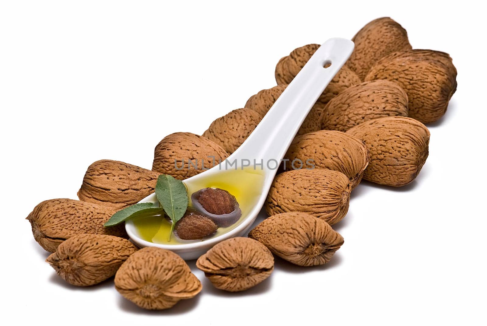 Almonds and a spoon with its oil over a white background.