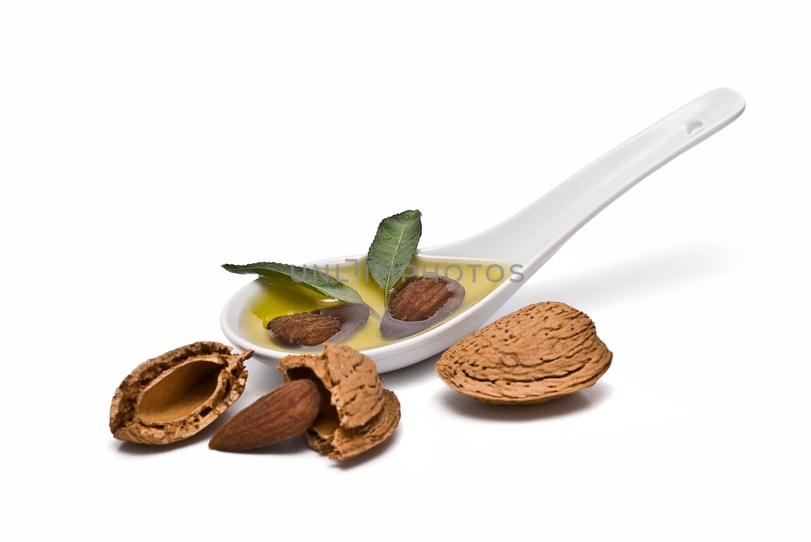 Almonds and a spoon with its oil over a white background.