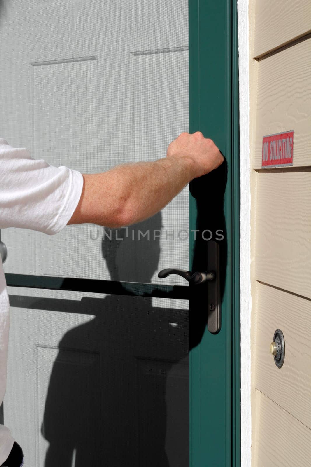 Male knocking on a residential front door during the day.