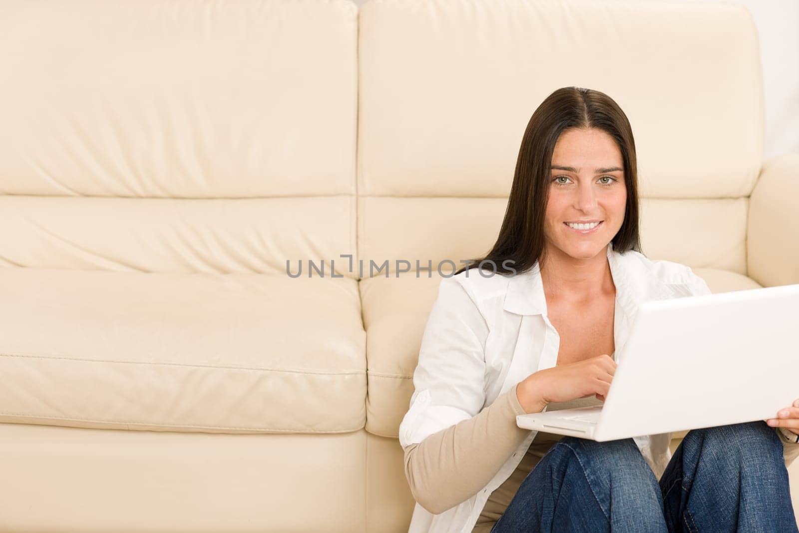 Attractive woman with laptop sitting by couch smiling