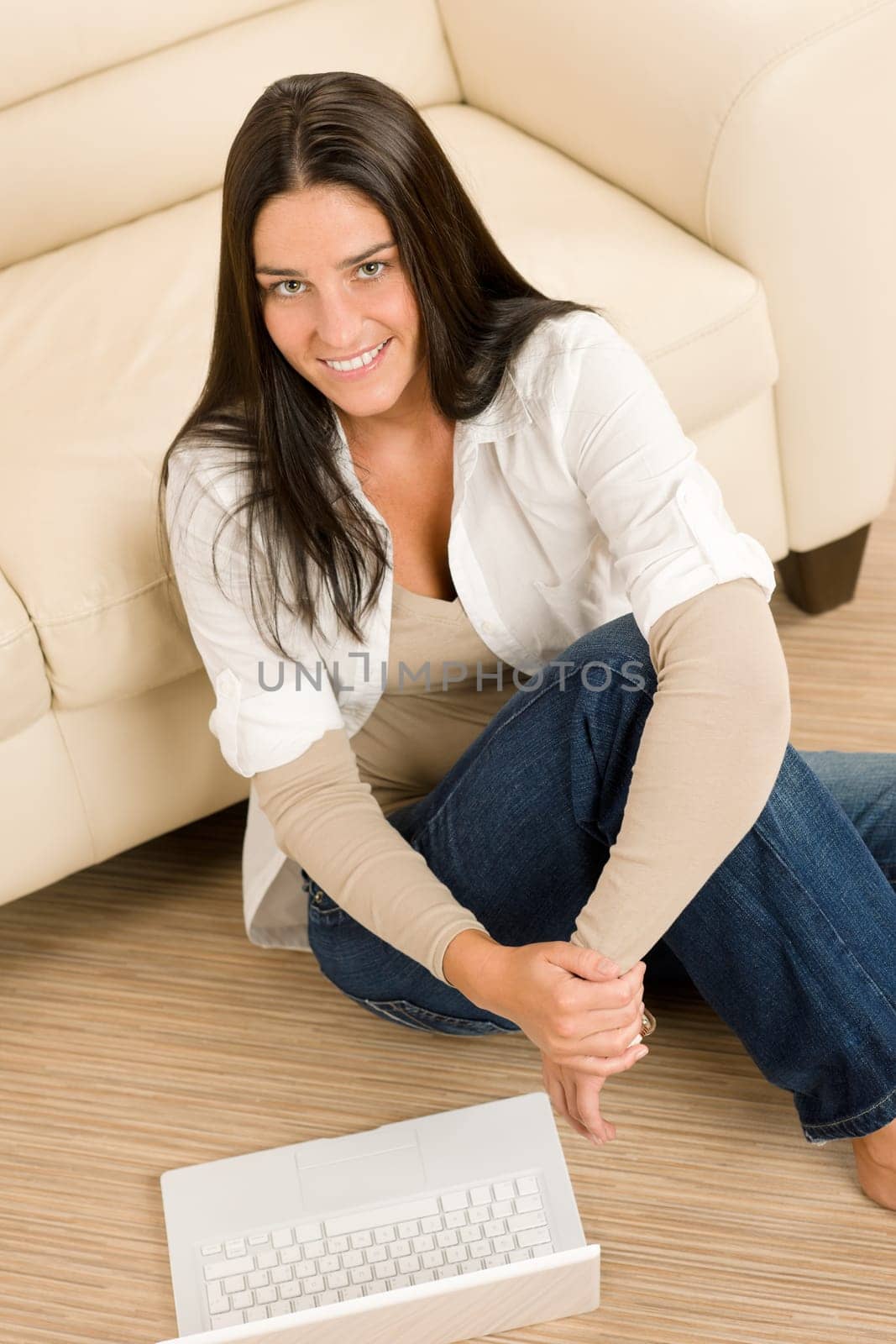 Attractive woman with laptop sitting by couch smiling