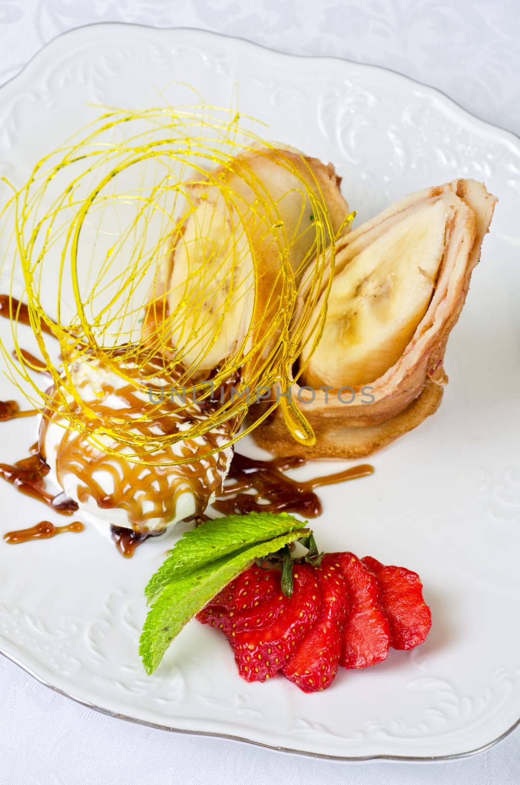 Dessert of pancake with banana, ice-cream, caramel, strawberry and mint