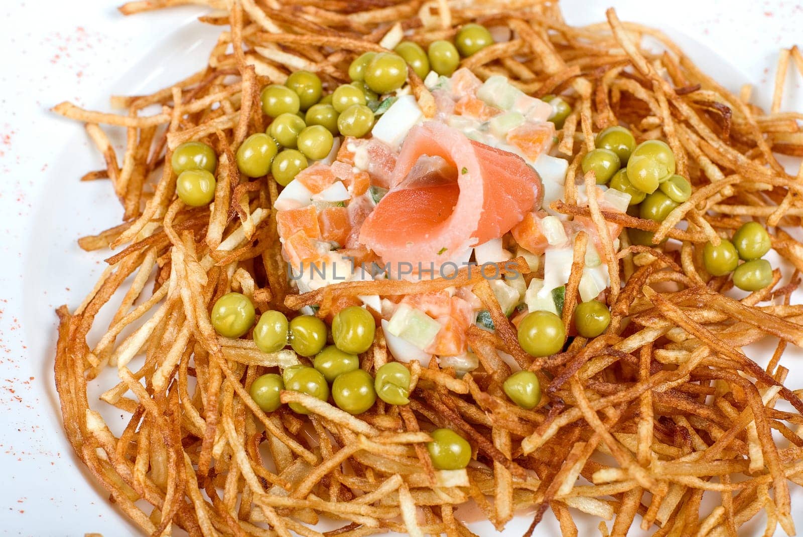 Closeup of salad with salmon fish at fried sliced potato with carrot and peas dressed by tomato sauce with cognac