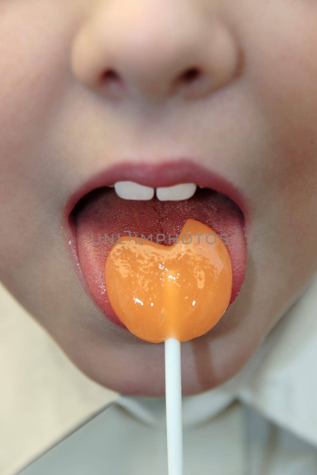 young girl licking an orange lollipop into a heart shape