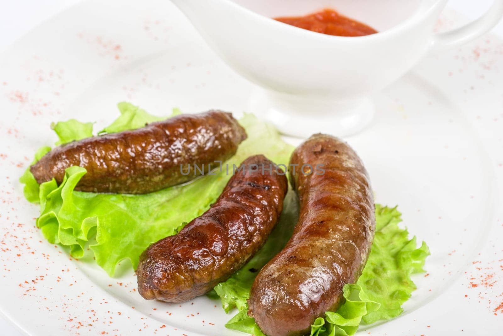 grilled venison sausage on a white with lettuce and sauce