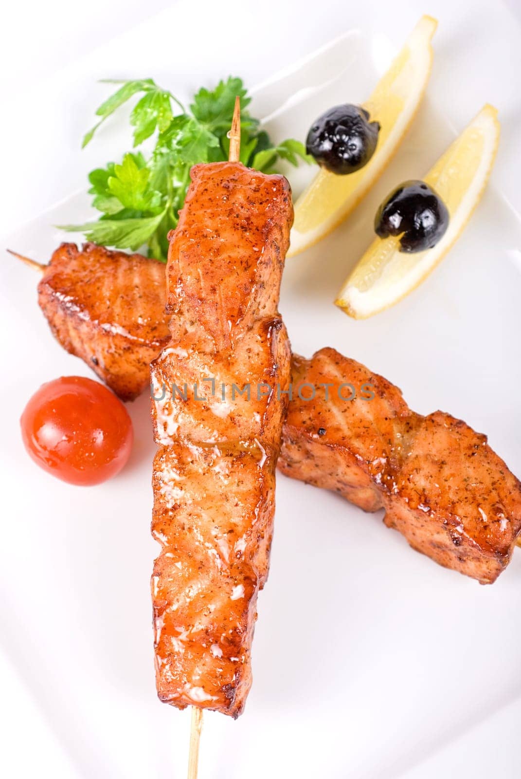 salmon kebab at plate with green lettuce and lemon on a white