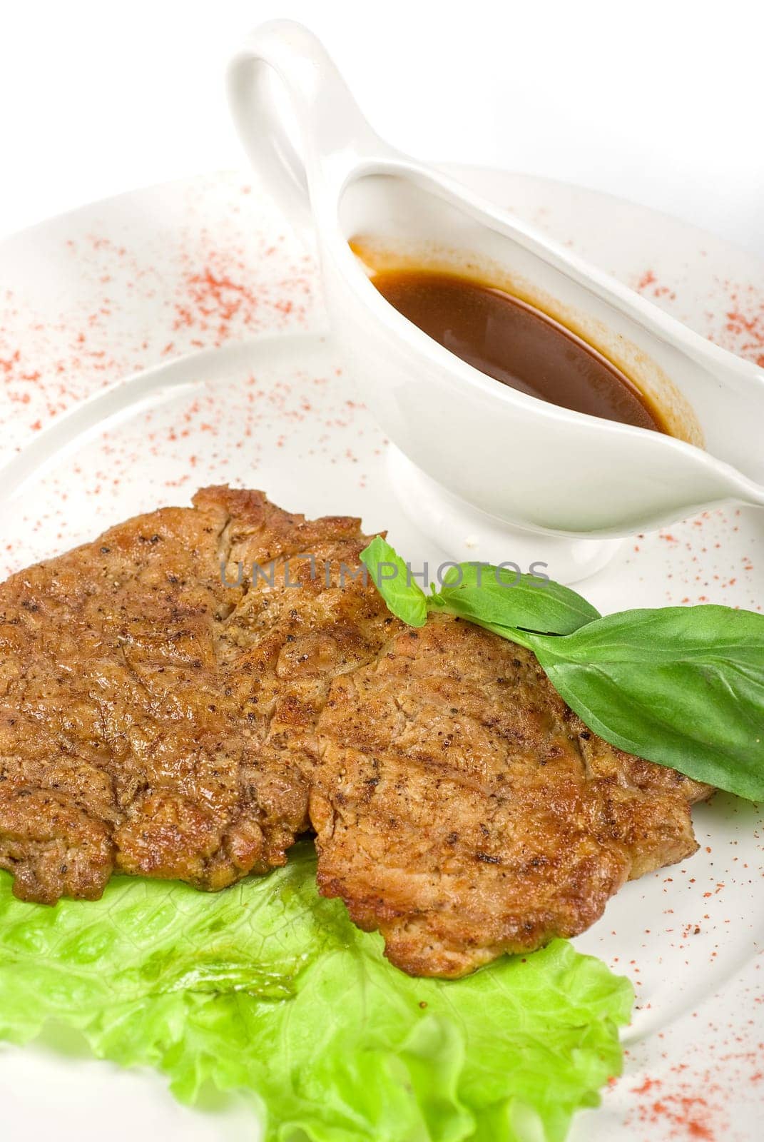 roasted pork steak at the white plate, with greens and sauce