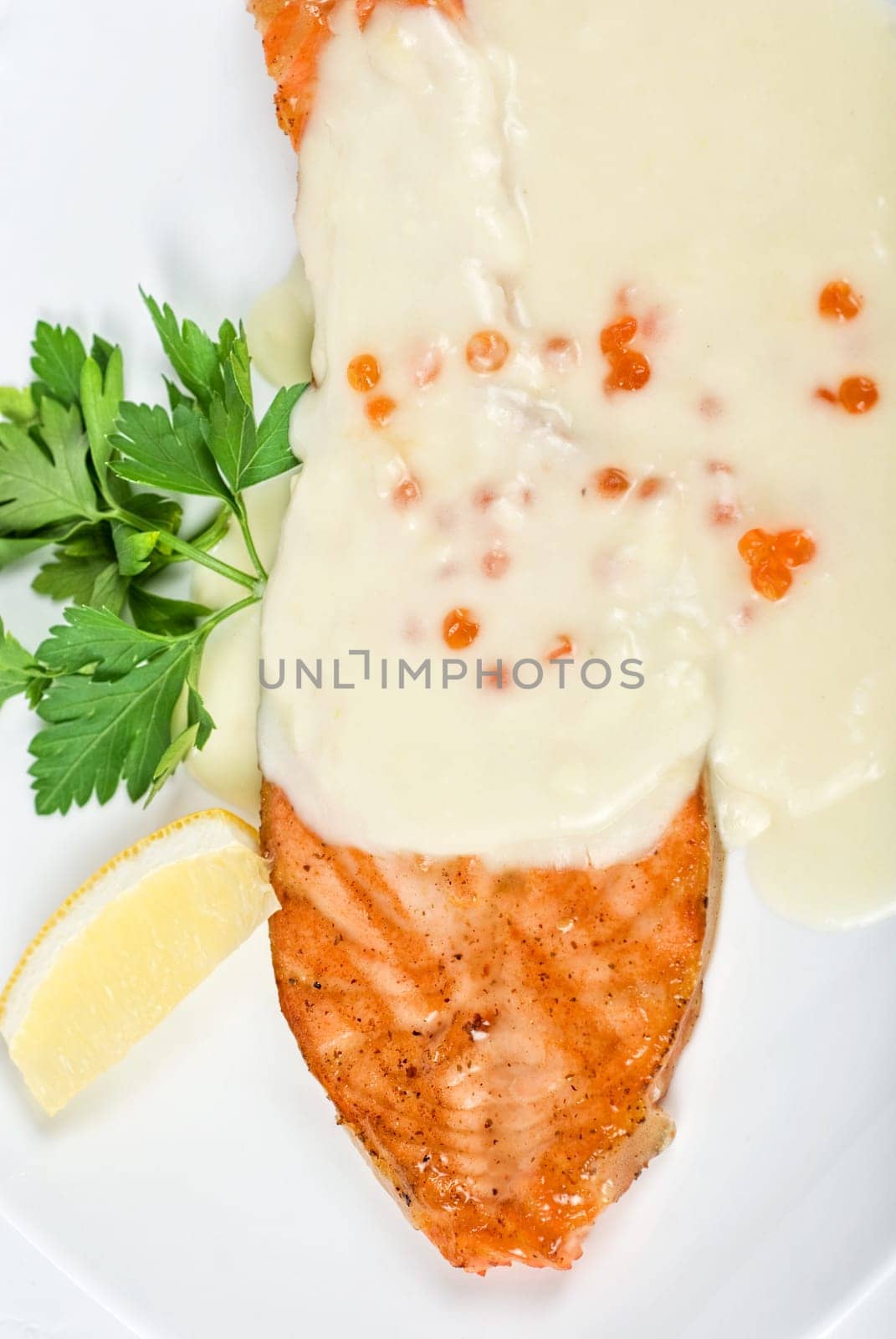 Grilled salmon steak with cheese sauce, greens, lemon and red caviar