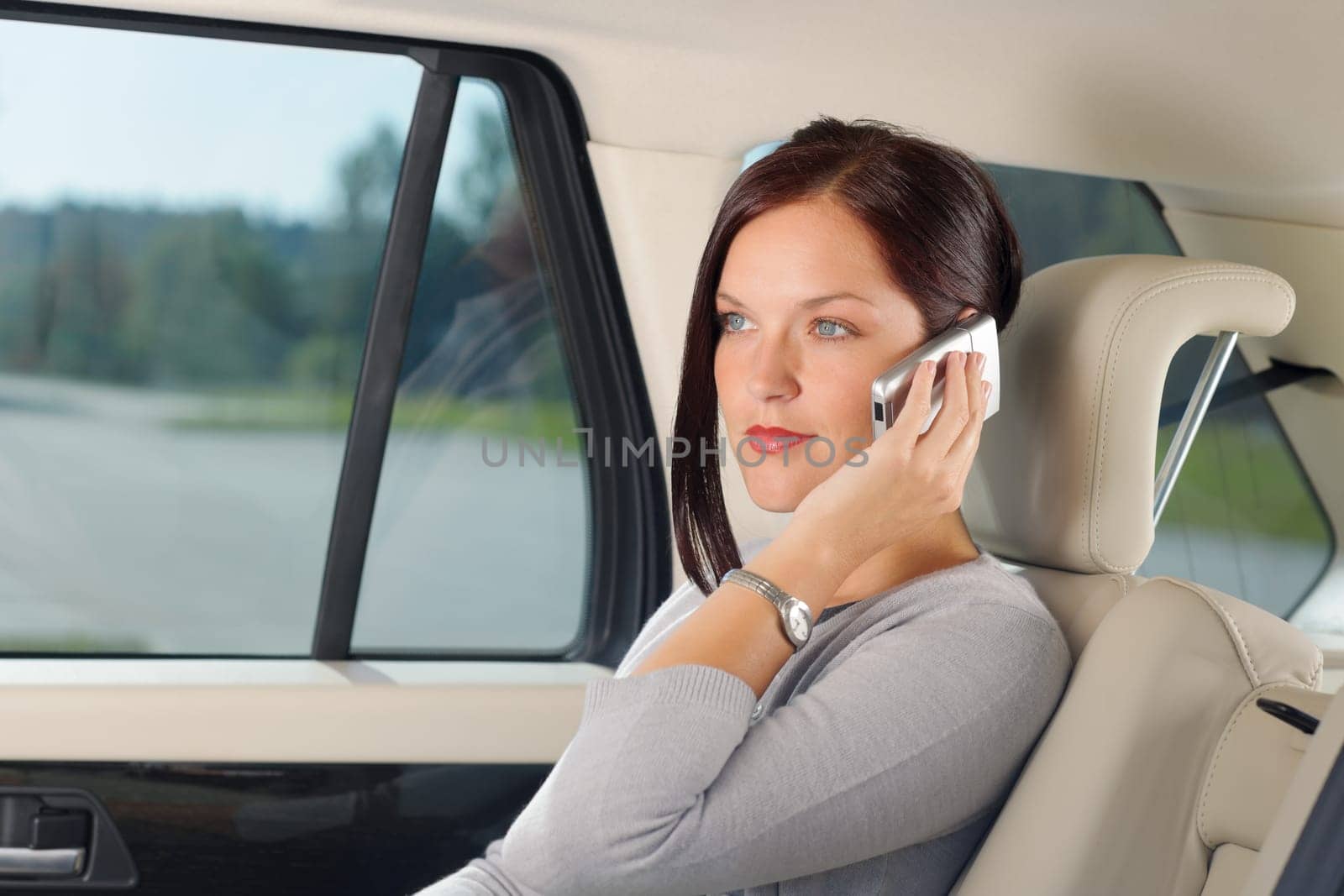 Executive attractive female manager sitting in car backseat calling phone