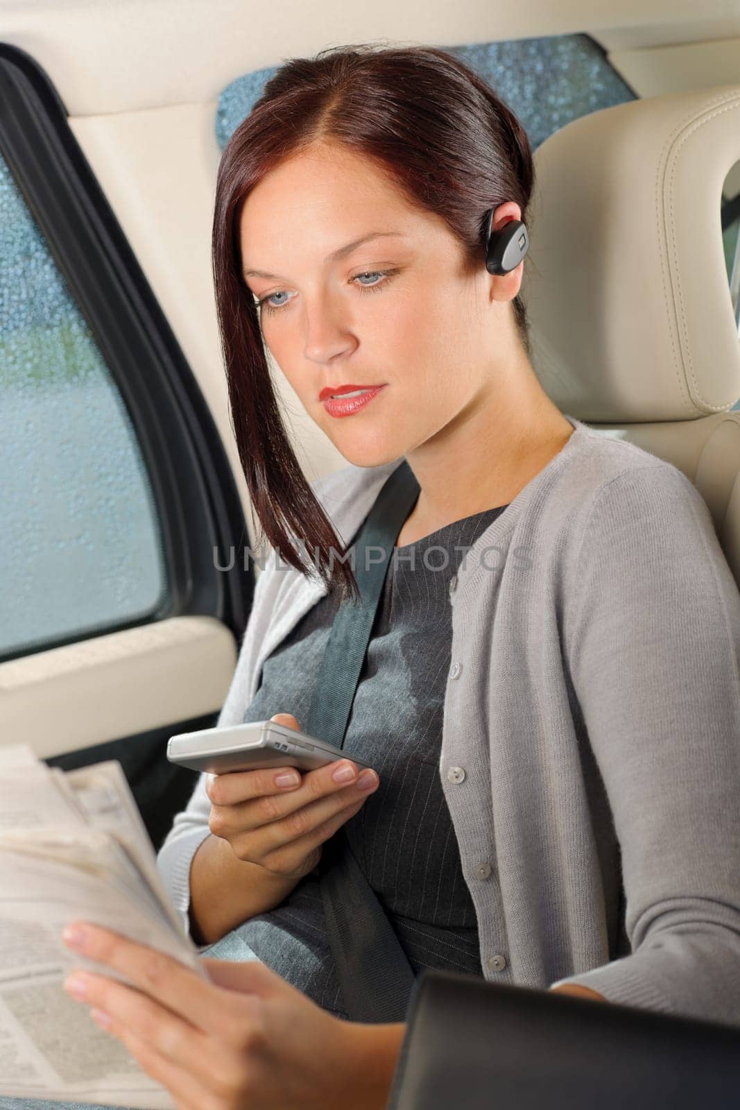 Attractive executive businesswoman sitting in car calling phone checking newspapers