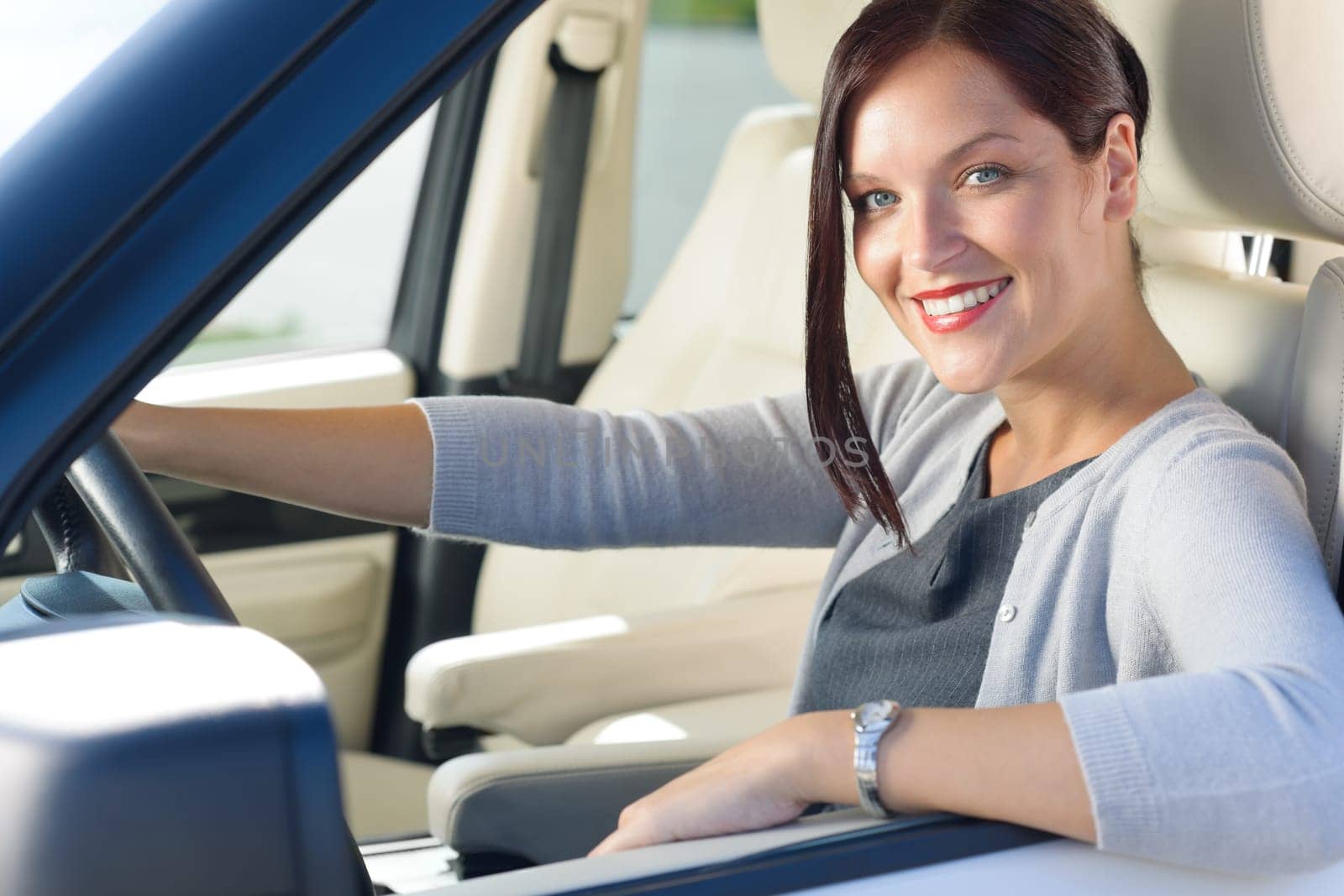 Attractive elegant businesswoman driving luxury car smiling at camera