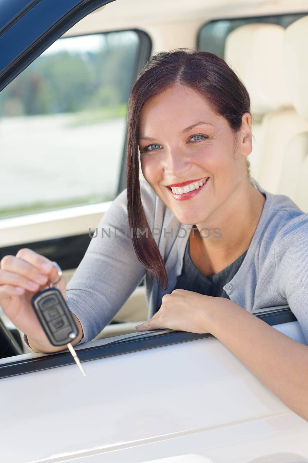 Attractive elegant businesswoman in new car showing keys smiling