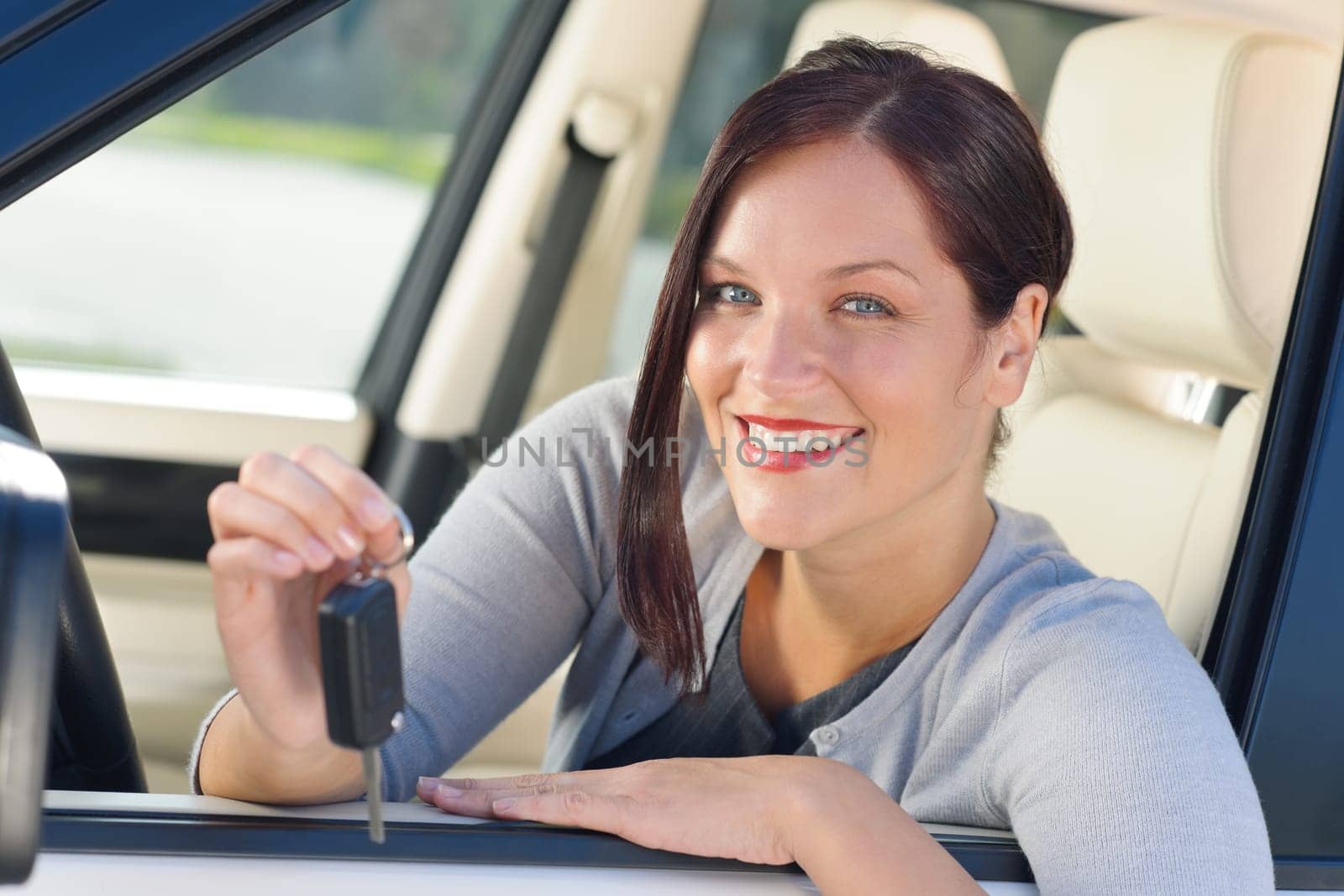 Attractive elegant businesswoman in new car showing keys smiling
