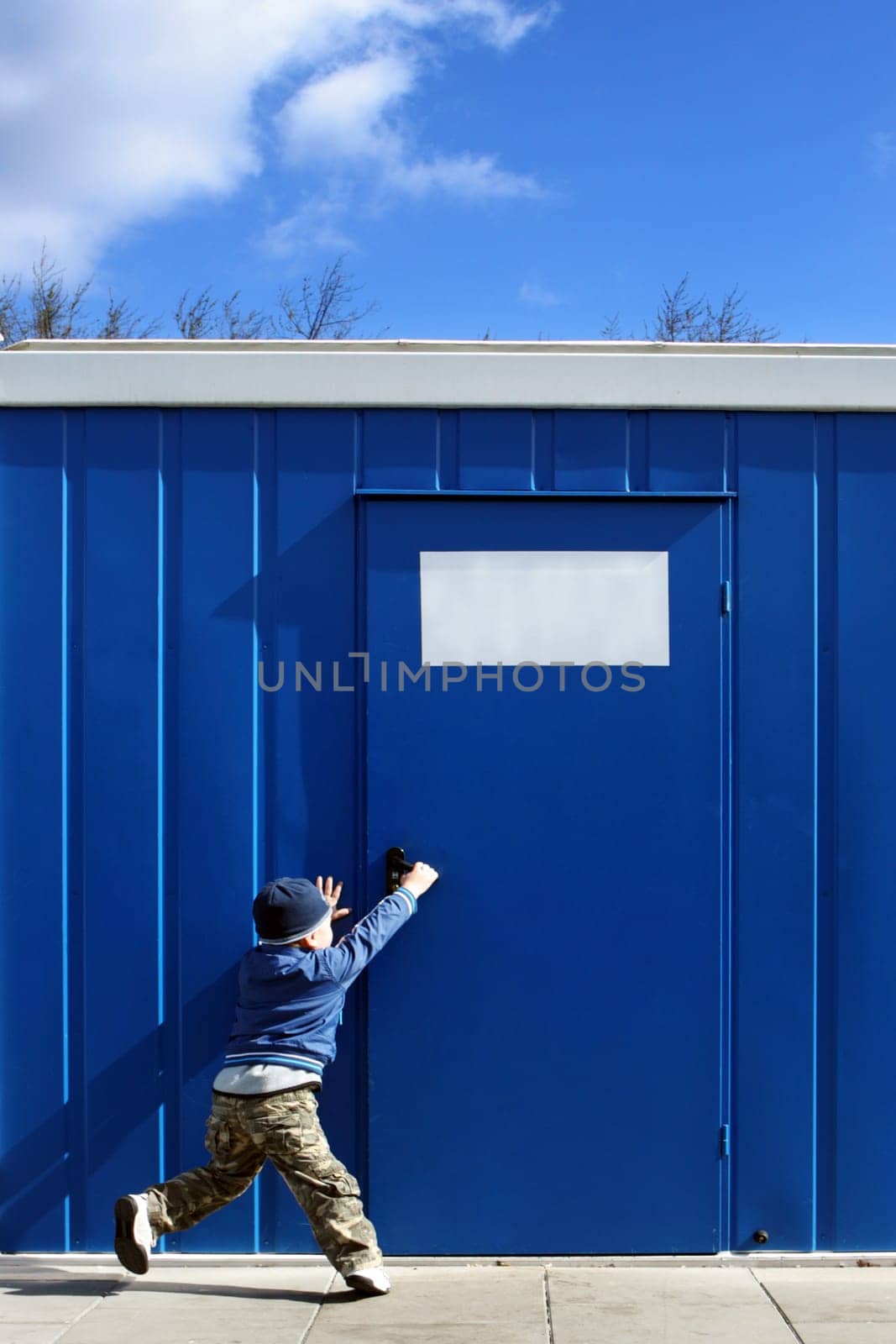 Baby boy wants to open the door handle near blue cellular homes.
