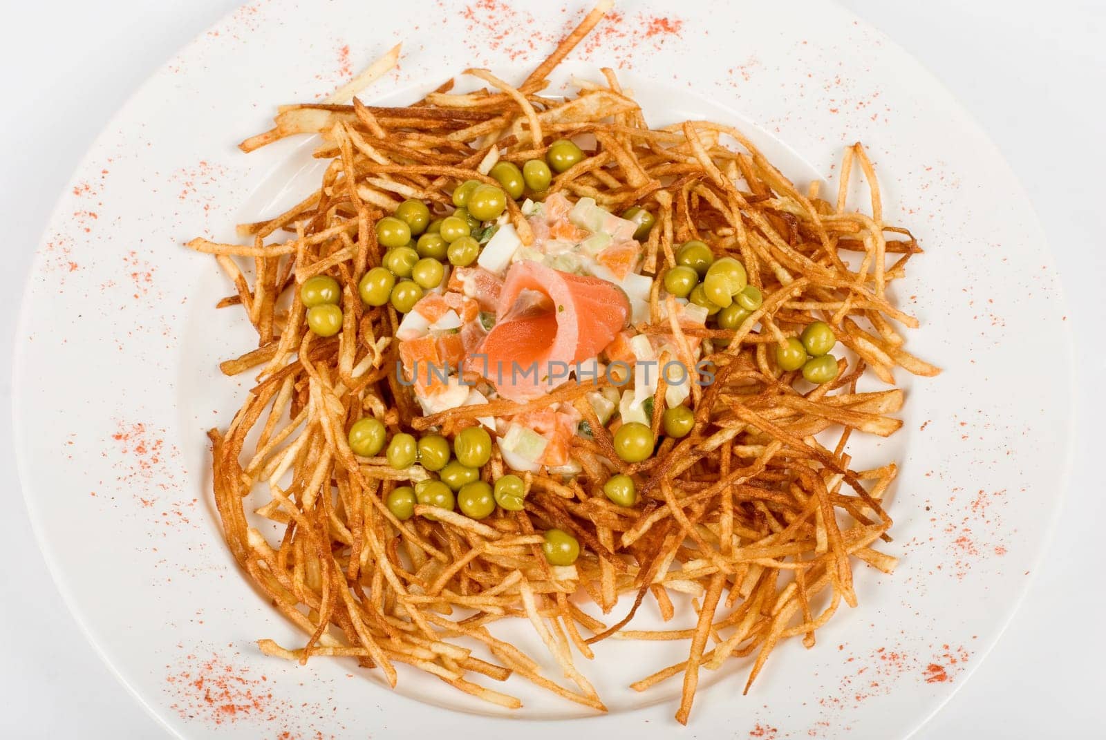 Closeup of salad with salmon fish at fried sliced potato with carrot and peas dressed by tomato sauce with cognac