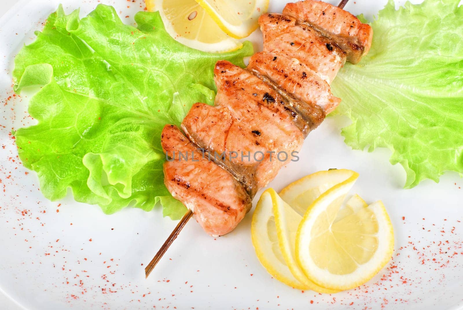 salmon kebab at plate with green lettuce and lemon on a white