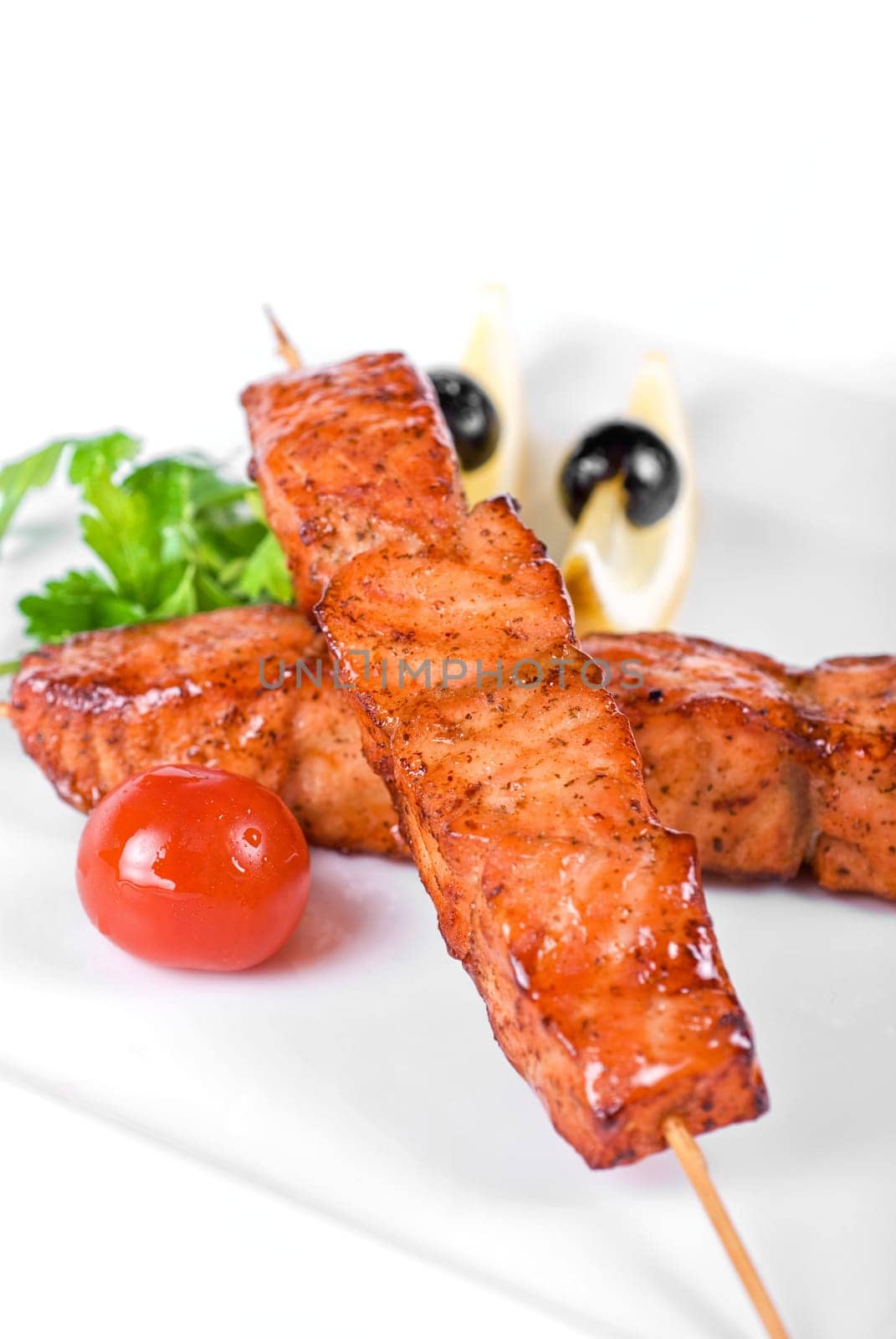salmon kebab at plate with green lettuce and lemon on a white