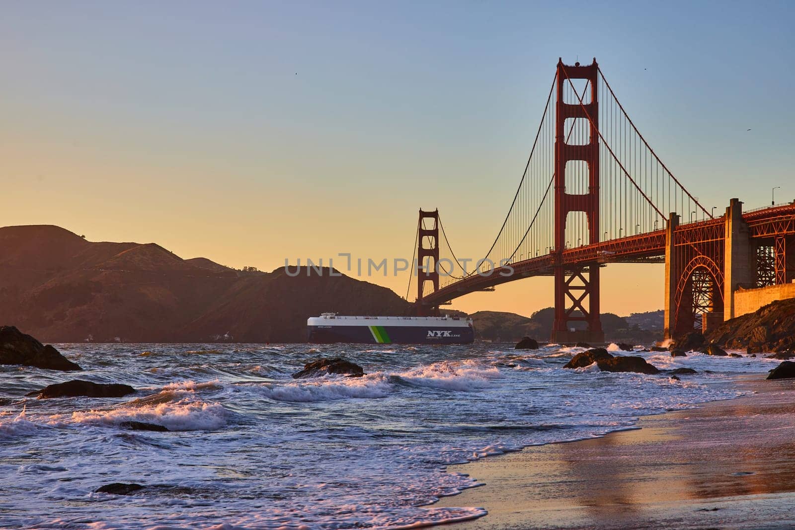Image of Ocean liner going under Golden Gate Bridge at sunset from sandy beach with waves