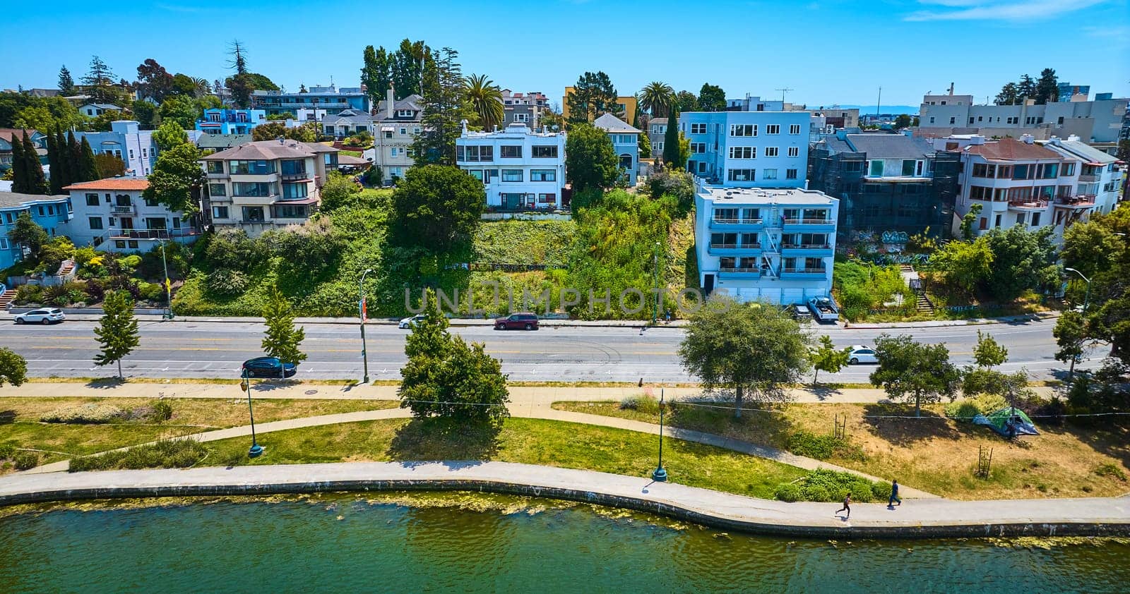 Image of Lake Merritt shoreline with joggers on pathway around lake aerial of apartment buildings