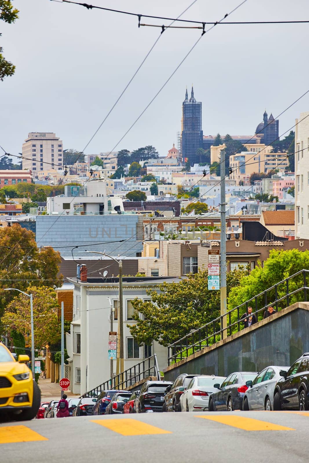 Image of Electric cables for green energy transportation going down steep hilly street with distant city