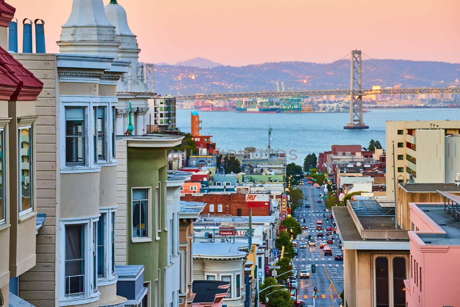 Image of Pink sunrise lighting over residential area of San Francisco with Oakland Bay Bridge and view of bay
