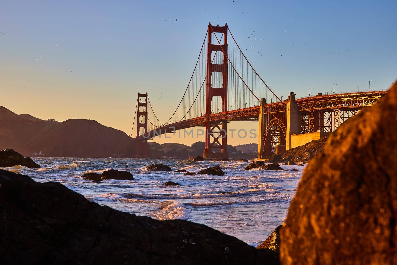 Image of Golden light on Golden Gate Bridge at sunset with view between boulders of bay