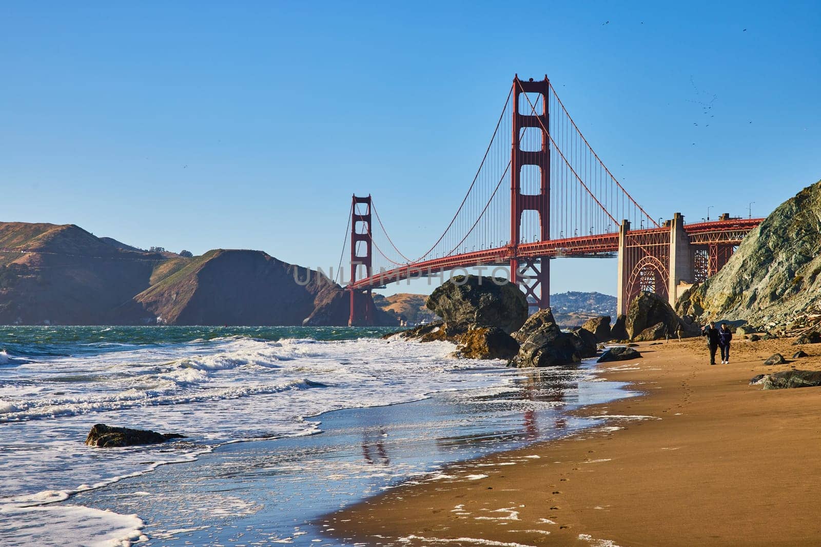 Image of Sandy beach with footprints leading to red Golden Gate Bridge