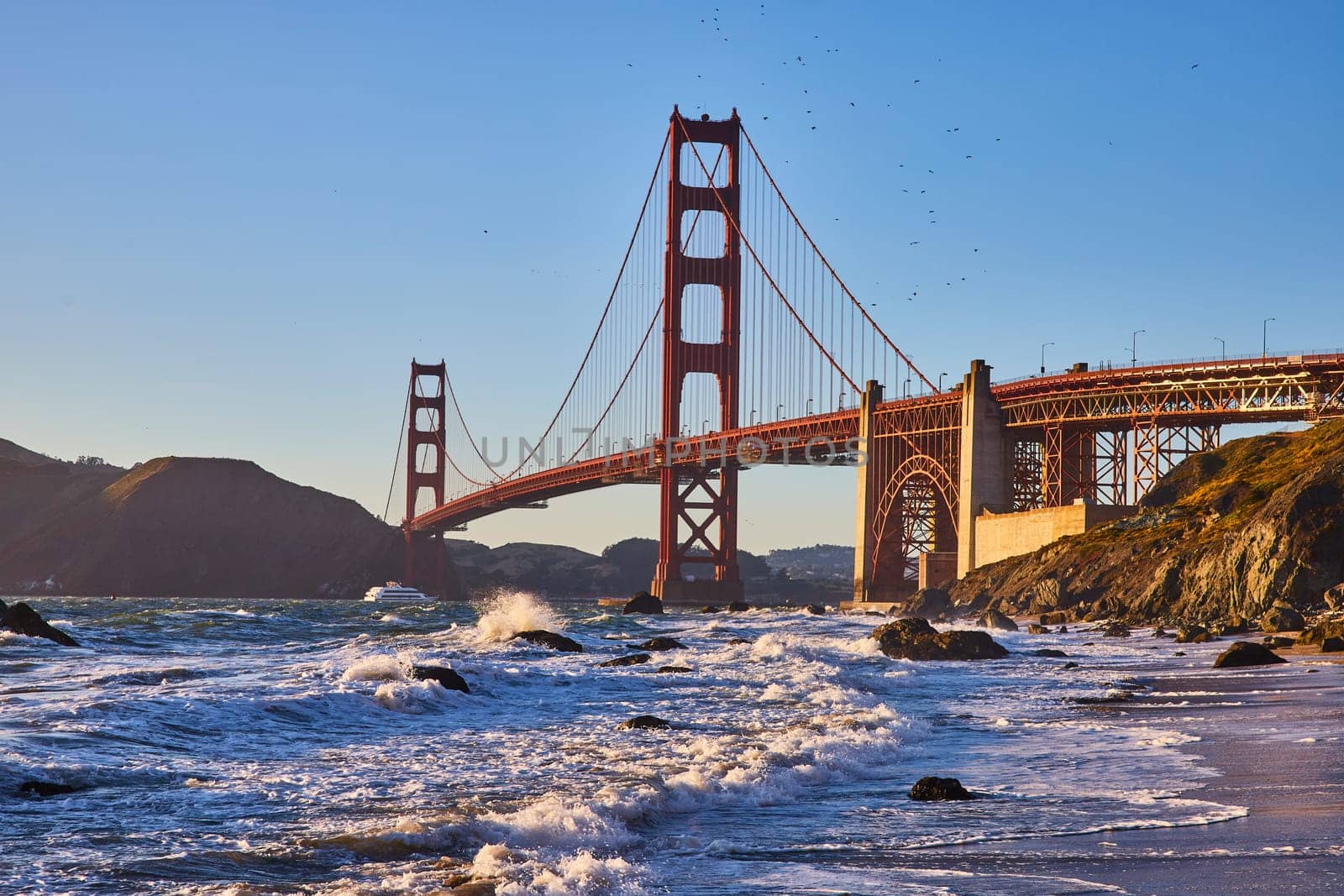 Image of Waves rolling into shore of sandy beach with view of Golden Gate Bridge at sunset