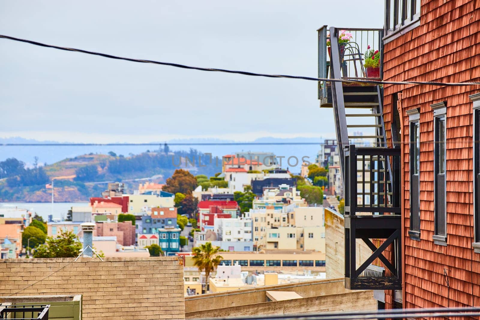 Image of Side of reddish brown building with black stairs and patio overlooking city buildings in California
