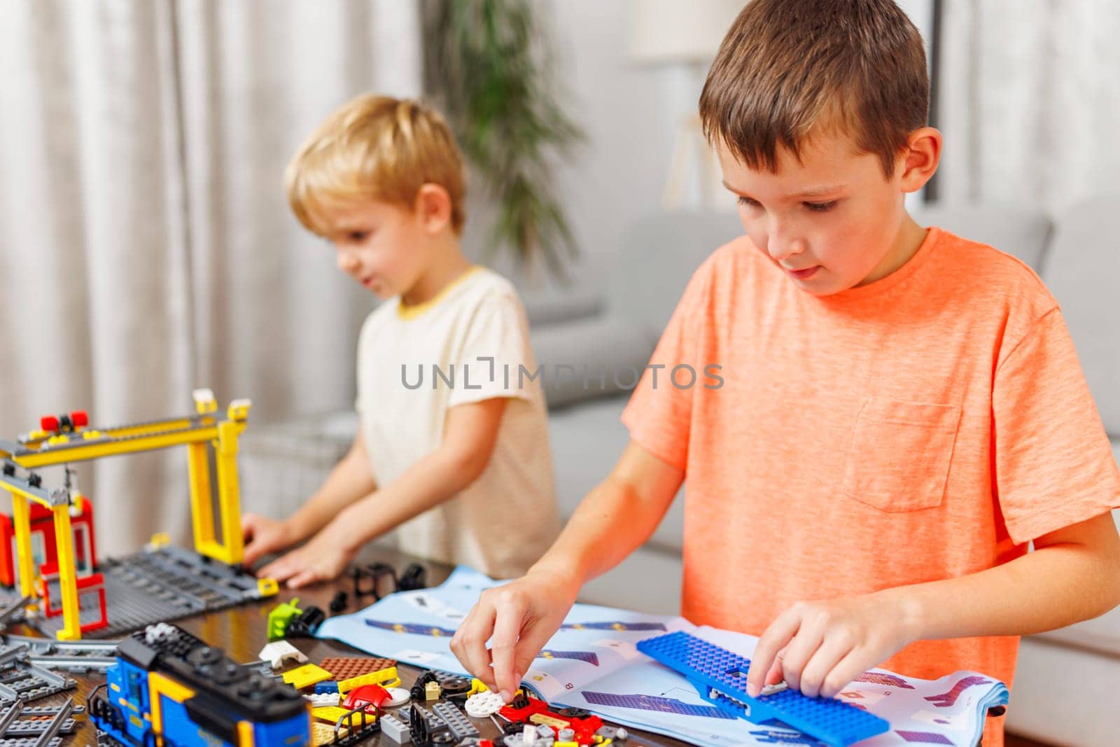 Two children playing and building with colorful plastic bricks at the table by andreyz