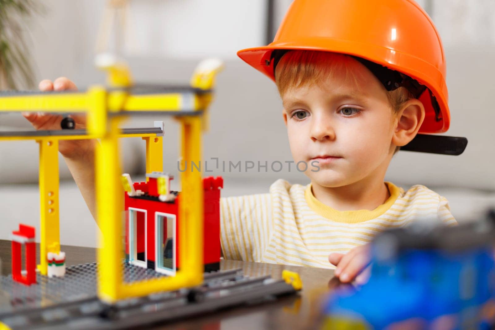 Child boy in helmet playing and building with colorful plastic bricks at the table. Early learning and development