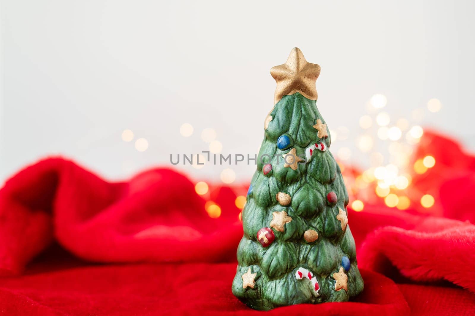 New Year's location with a green toy fir tree standing on a red blanket against a bokeh background with a garland of lights. Place for an inscription