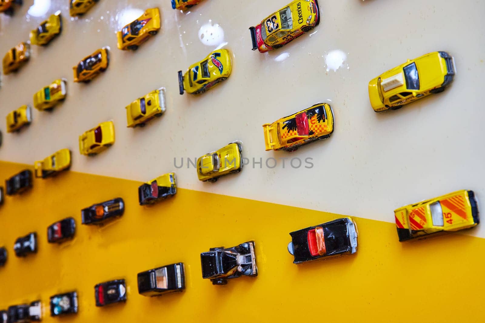 Image of Toy cars in black and yellow colors on shiny wall split diagonally between white and yellow
