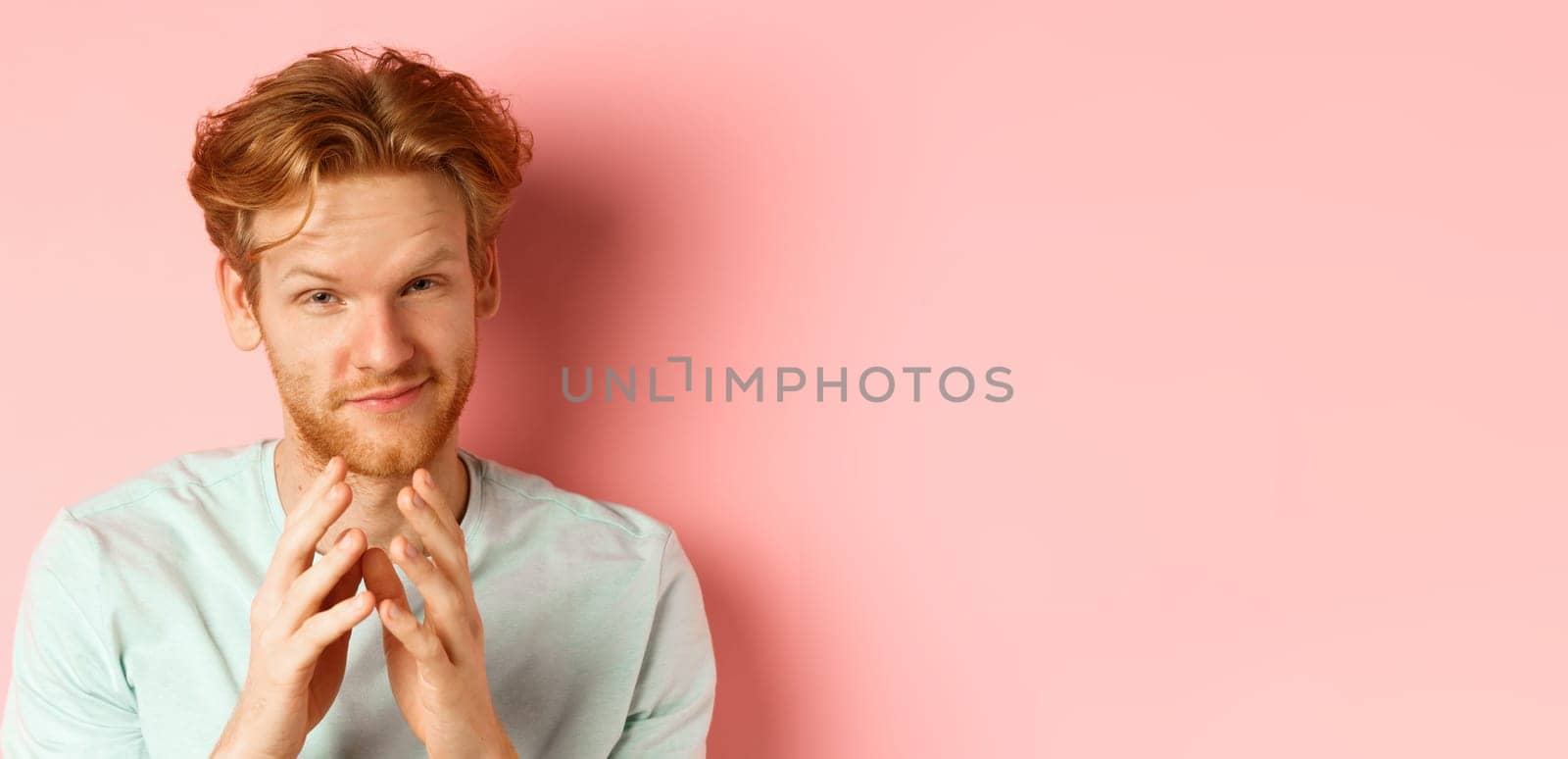 Close up of funny bearded man with red hair pitching a perfect plan, smiling and steeple fingers, scheming something, standing devious against pink background.