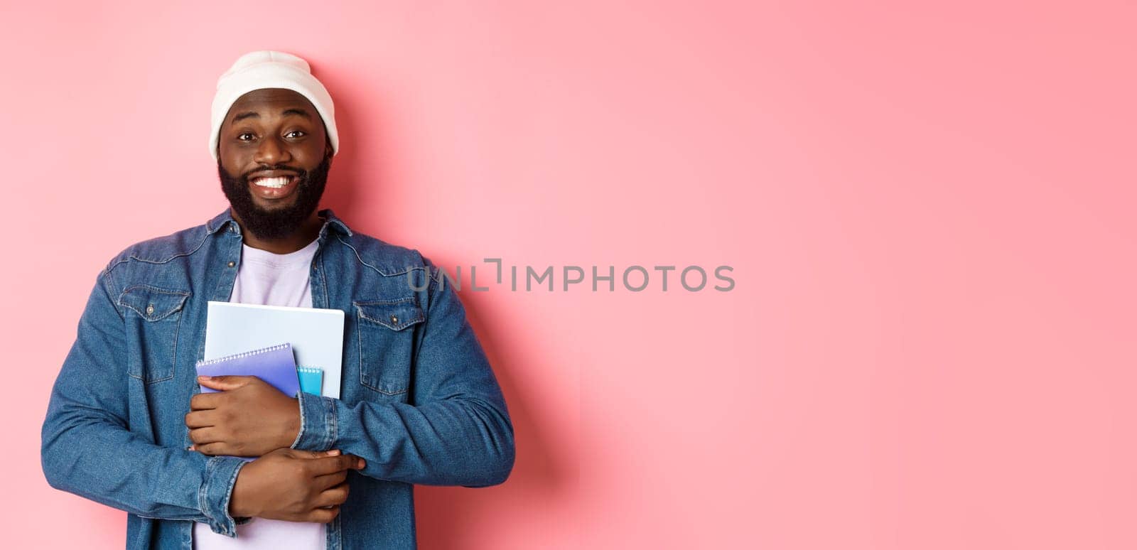 Image of adult Black man holding notebooks and smiling, studying at courses, standing over pink background.