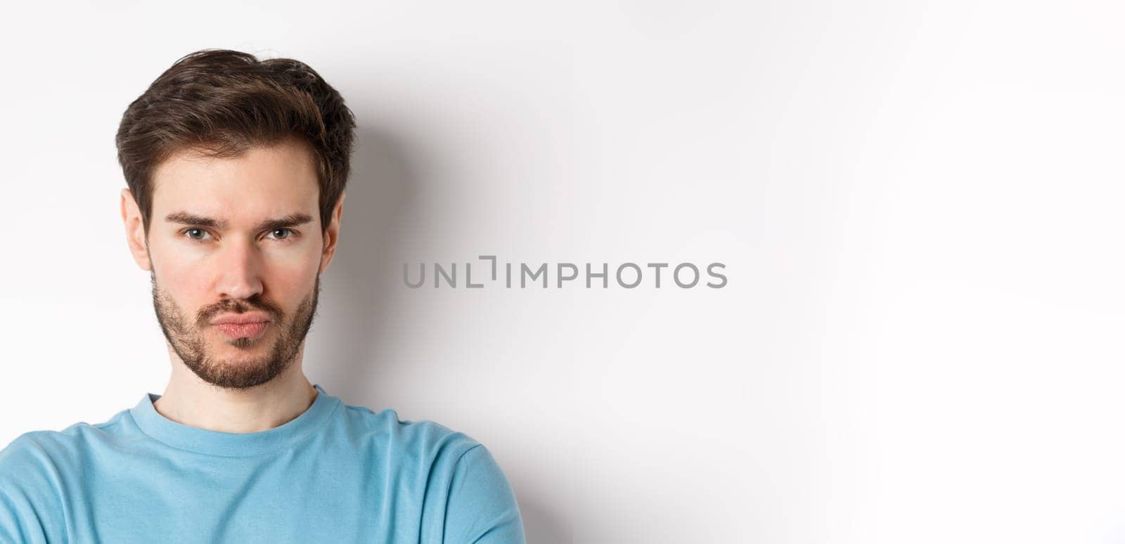 Close-up of grumpy young man grimacing, sulking and making offended face, standing upset over white background.
