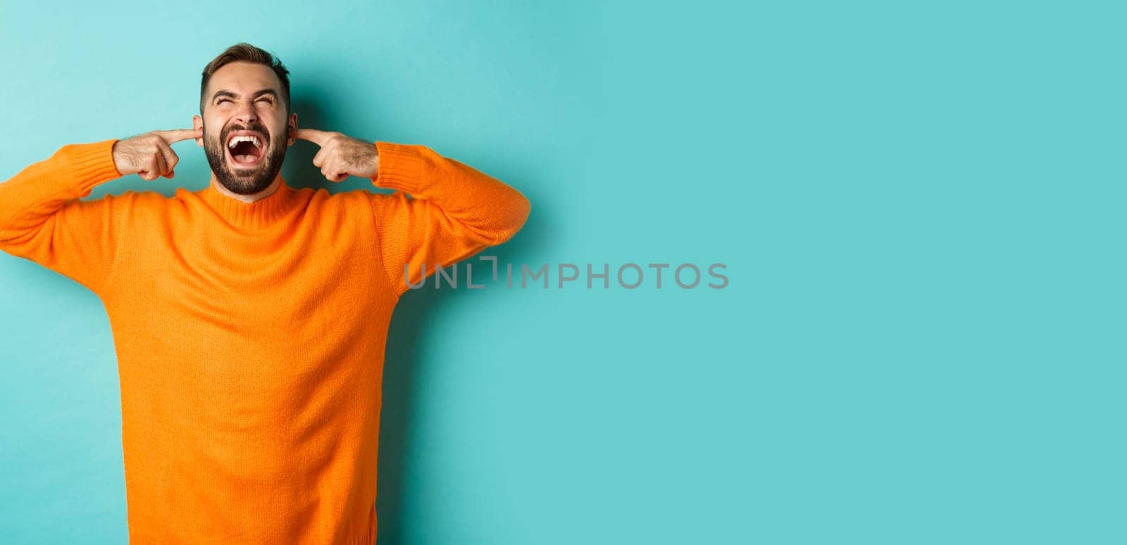 Frustrated and annoyed man shouting at neighbours upstairs, shut ears with fingers, loud bothering noise, standing over light blue background by Benzoix