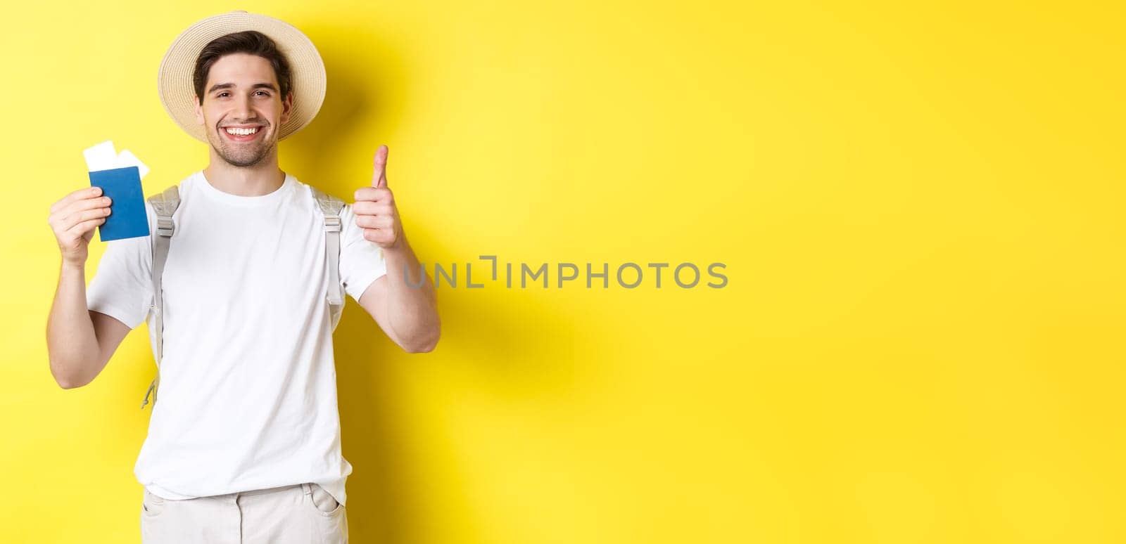 Tourism and vacation. Satisfied male tourist showing passport with tickets and thumb up, recommending travel company, standing over yellow background by Benzoix