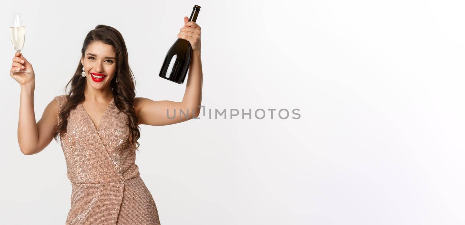 Winter holidays celebration concept. Excited beautiful woman in dress raising glass of champagne for toast, enjoying Christmas party, standig over white background.