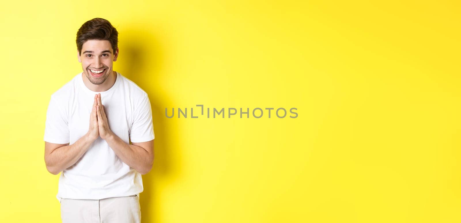 Handsome guy saying thank you, bowing and holding hands in namaste gesture, express gratitude, standing over yellow background.