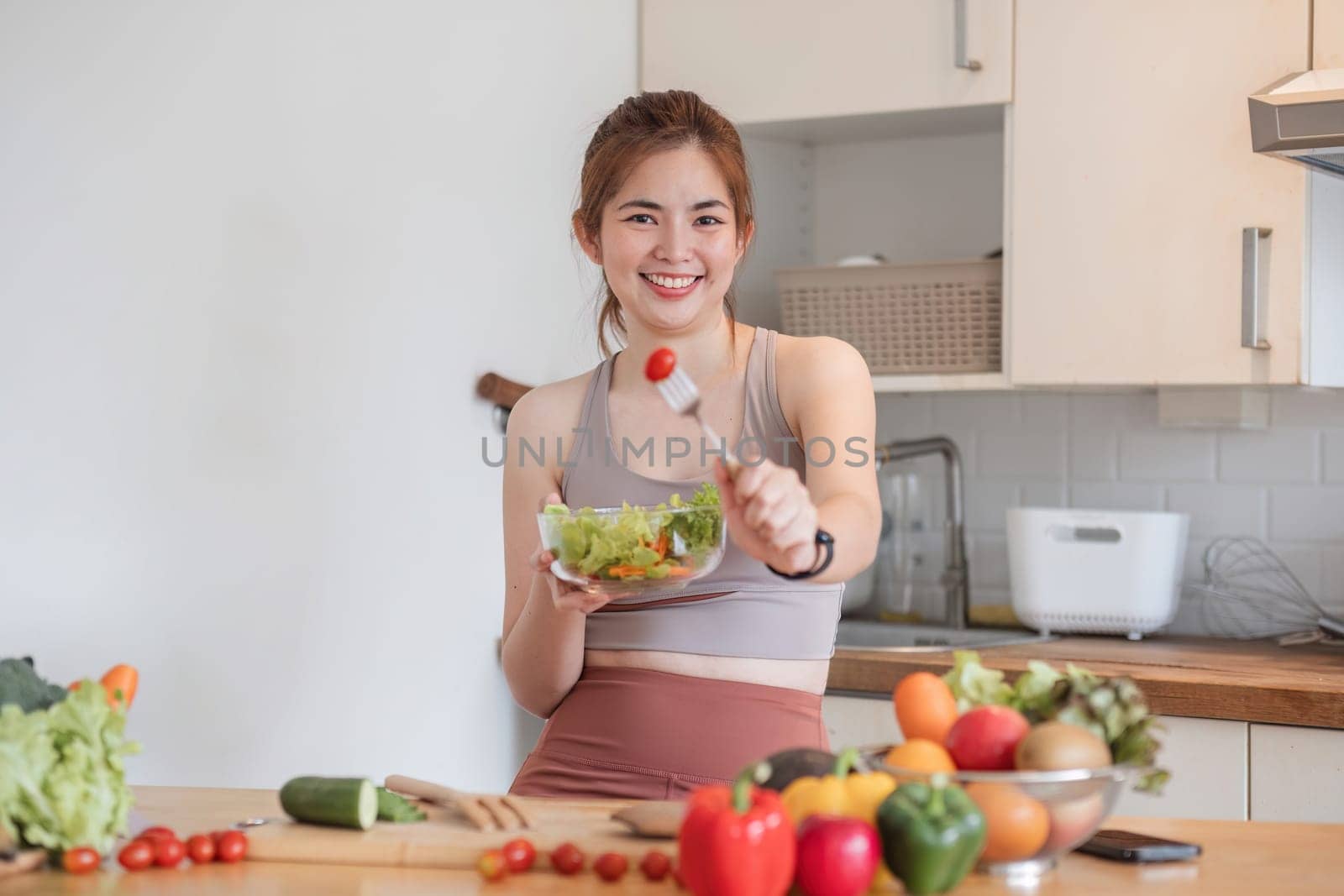 Young athletic woman is preparing a healthy organic vegetable salad in a modern kitchen at home. by wichayada