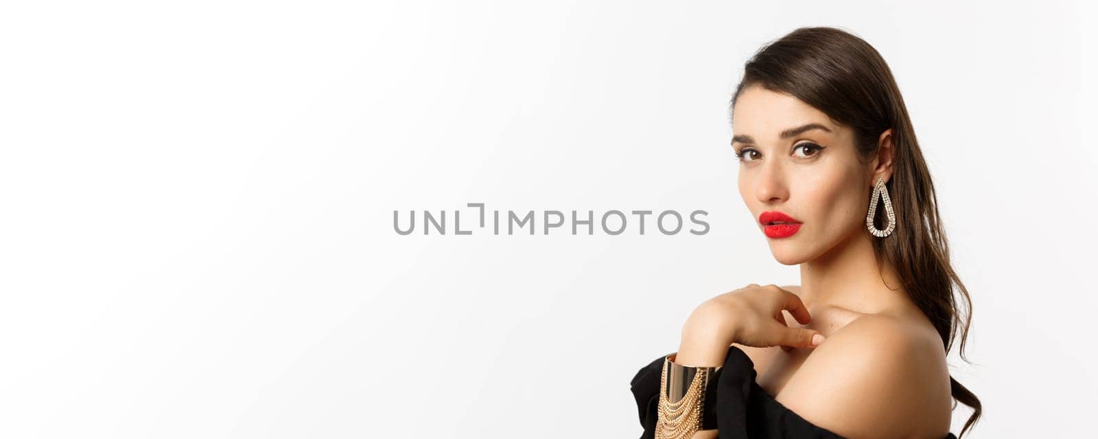 Fashion and beauty concept. Close-up of elegant woman with red lips, makeup and earrings, looking at camera self-assured, standing over white background by Benzoix