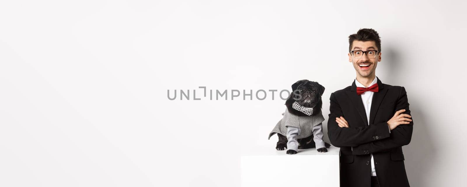 Animals, party and celebration concept. Happy dog owner in suit and puppy in costume looking excited at camera, having fun, standing over white background.