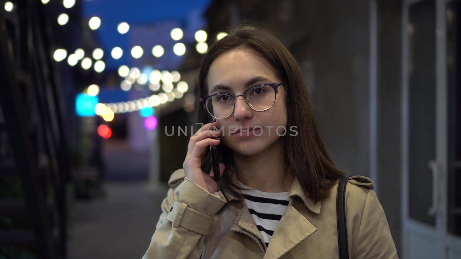 A young woman talks on the phone late at night on a narrow street. A girl with glasses communicates on a mobile phone. 4k