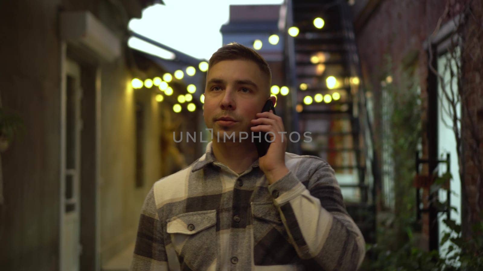 A young man is talking on the phone and walking along a narrow street. A man is on the street late at night with a phone. 4k