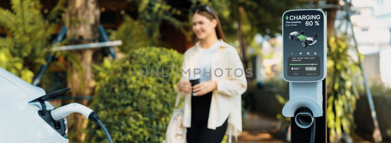 Young woman with coffee cup and sustainable urban commute with EV electric car recharging at outdoor coffee cafe in springtime garden, green city and environmental friendly EV car. Panorama Expedient