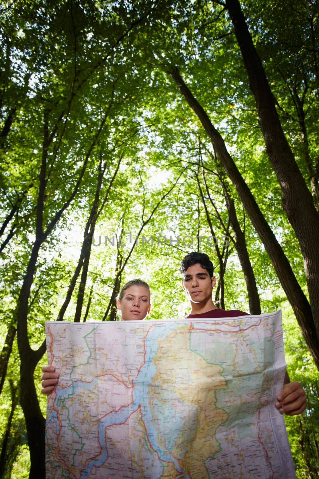 young man and woman checking map during hiking excursion and look for destination. Vertical shape, low angle view
