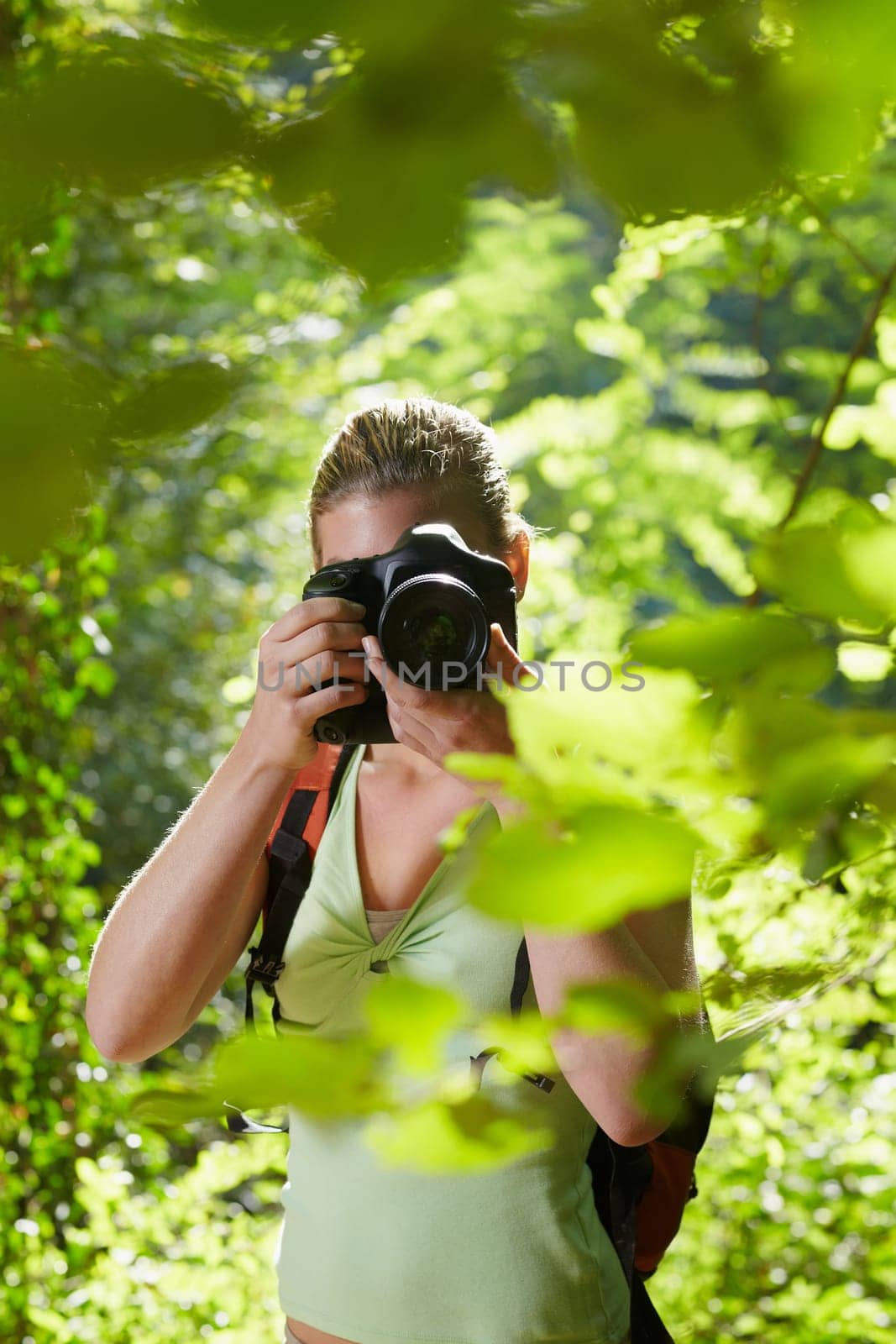 young woman trekking among trees and taking pictures with dslr camera. Vertical shape, front view, waist up