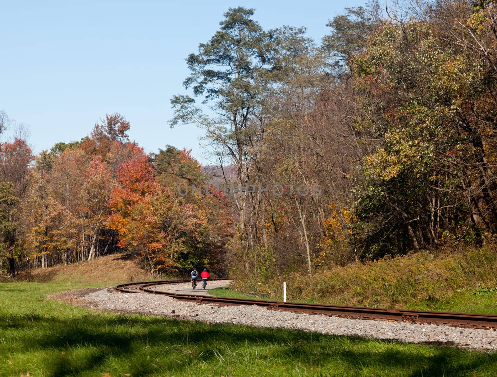 Two cyclists ride bikes down besides old railway line in rural countryside