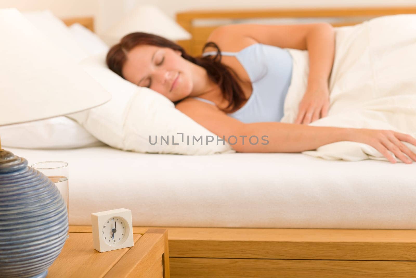 Alarm clock on bedside table woman sleeping in white bed